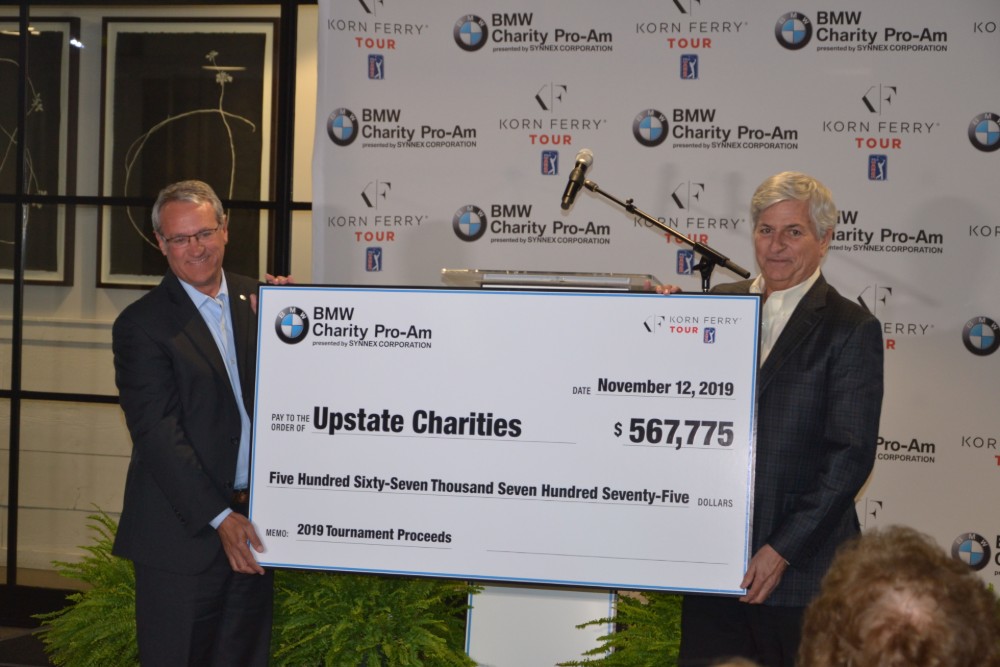 Max Metcalf, left, and Bob Stegner unveil and present a check representing the funds to be divided among four charities from the 2019 tournament. (Photo/Ross Norton)